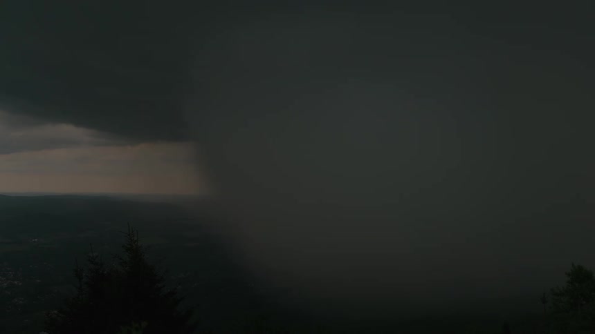 A dark and ominous rain shaft from a severe thunderstorm moves across the landscape, with lightning flashing within the clouds