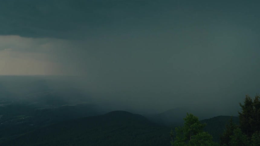 A powerful lightning strike flashes across the sky during a heavy thunderstorm over a misty mountain range