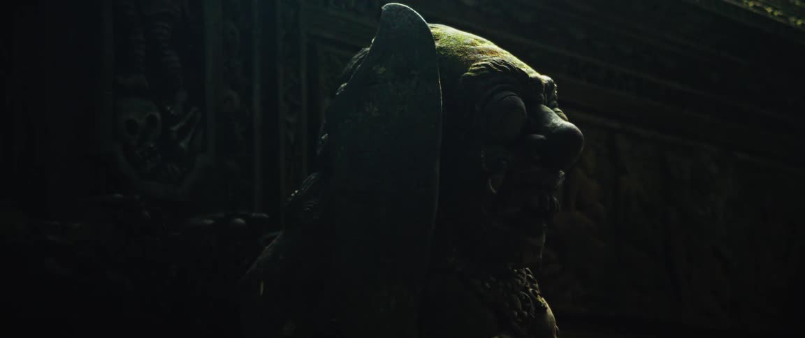 A menacing, moss-covered stone guardian statue is revealed by a sliver of light within a dark, ancient temple