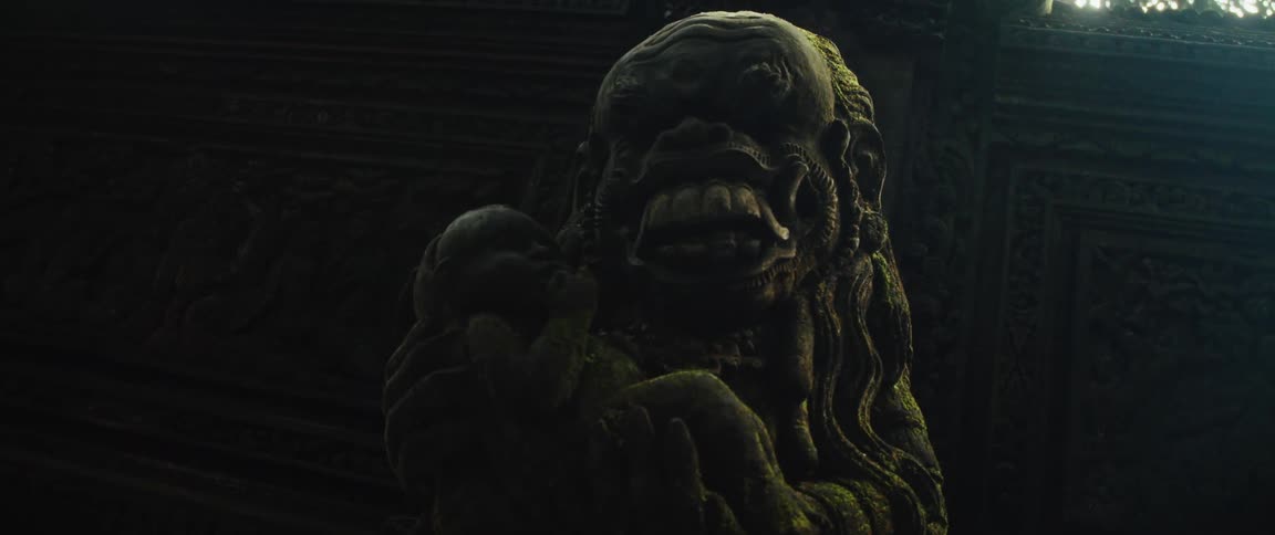 A slow zoom reveals a dark and mossy ancient stone statue of a demon holding a baby inside a mysterious temple