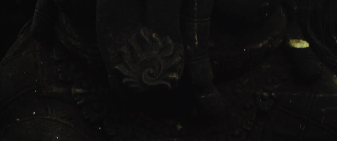 A slow pan reveals ancient, moss-covered stone carvings of skulls and a demonic face in a dark temple
