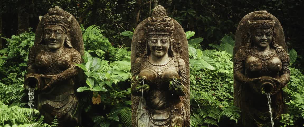 Ancient Balinese goddess statues act as a fountain in a lush tropical jungle
