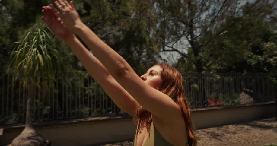 Close up slow motion of a woman raising her arms in a yoga pose while practicing outdoors in a lush garden