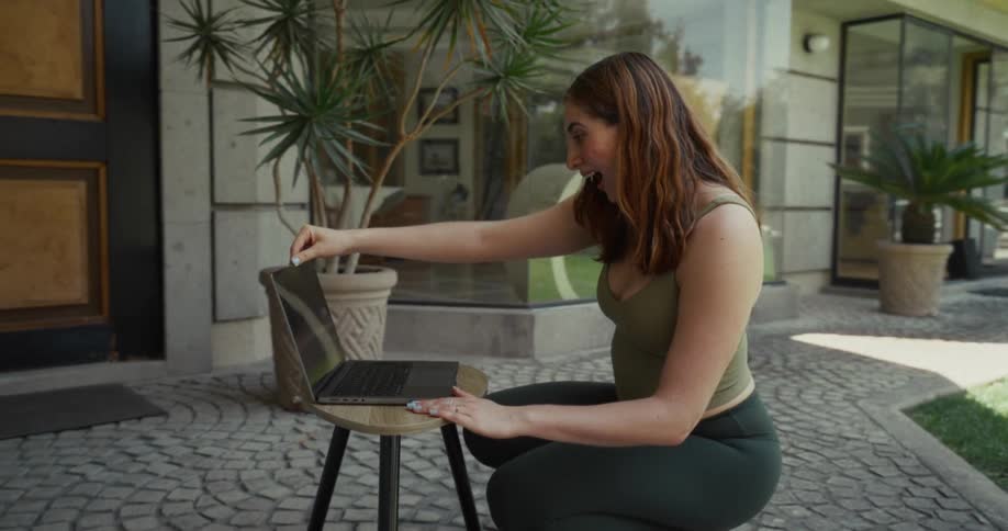 Slow motion side view of an astonished woman in athletic wear opening a laptop on a sunny patio