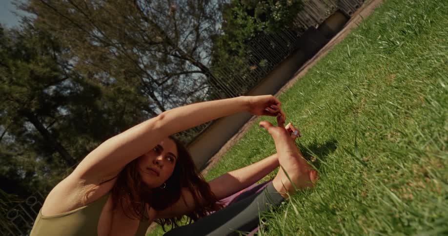 A young woman gracefully holds a deep seated yoga stretch on a mat in a sun-drenched grassy yard