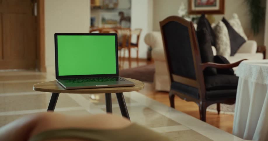 A woman follows an online yoga class in her living room, with the green screen laptop in focus as she stretches on the floor