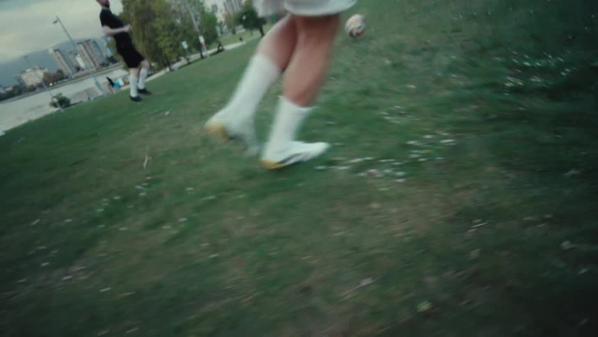 Dynamic, slow-motion, low-angle tracking shot of a soccer player's feet as they dribble the ball across a grassy park
