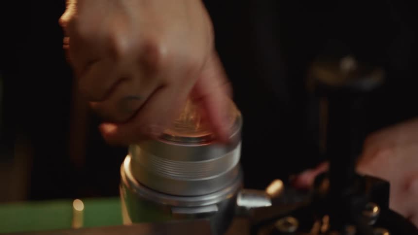 A close-up of a barista with a moon tattoo on her finger tamping coffee grounds in a portafilter
