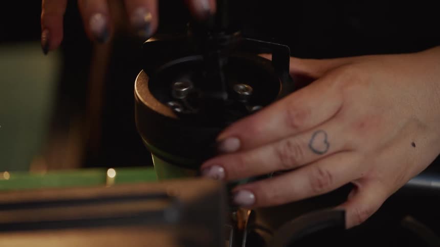 A barista's hands are seen in a close-up, slow-motion shot as they use a coffee distribution tool on a portafilter filled with fresh coffee grounds