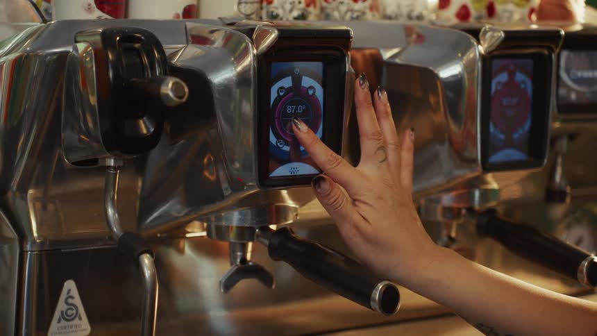 A close-up shot of a barista's hand adjusting the settings on the digital touchscreen of a modern espresso machine