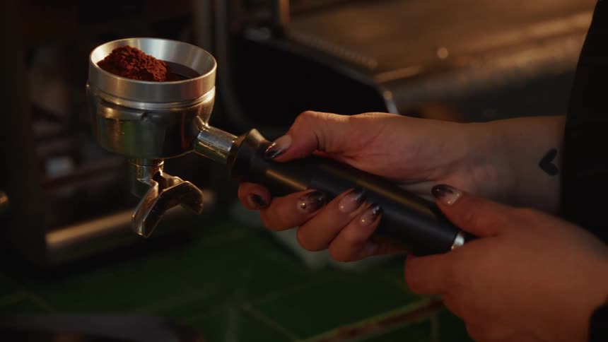 Slow motion close up of a barista's tattooed hand holding a portafilter filled with fresh coffee grounds