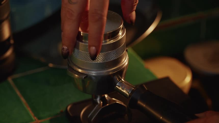 A barista uses a metal coffee distribution tool to level fresh coffee grounds in a portafilter