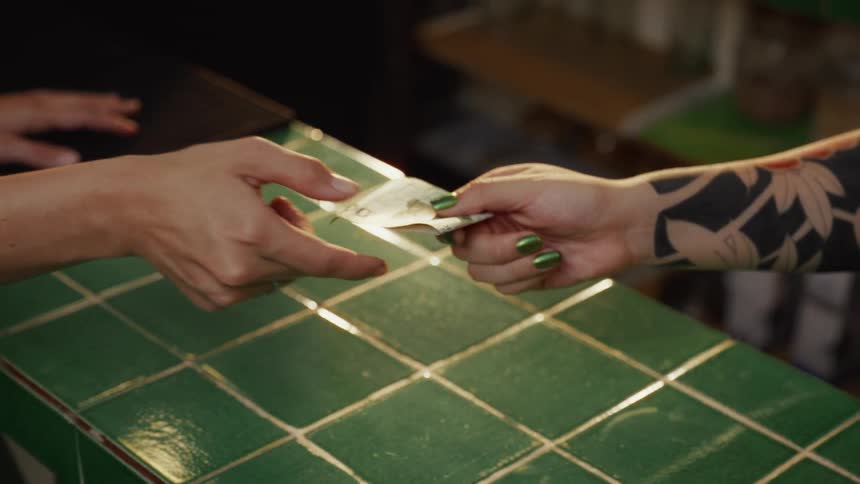 A close-up slow motion shot of a woman handing a 200 peso bill to a tattooed cashier with green fingernails