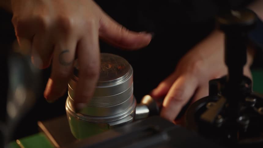 A barista with tattoos uses a distribution tool and tamper to prepare espresso grounds in a portafilter