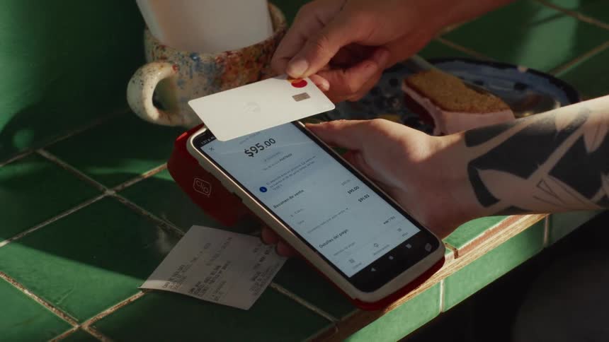 Close-up of a customer paying with a tap-to-pay credit card on a smartphone payment terminal at a cafe counter