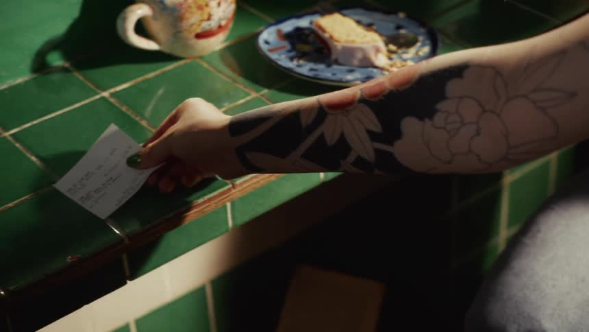 Slow-motion close-up of a tattooed person placing a receipt on a green tiled cafe counter