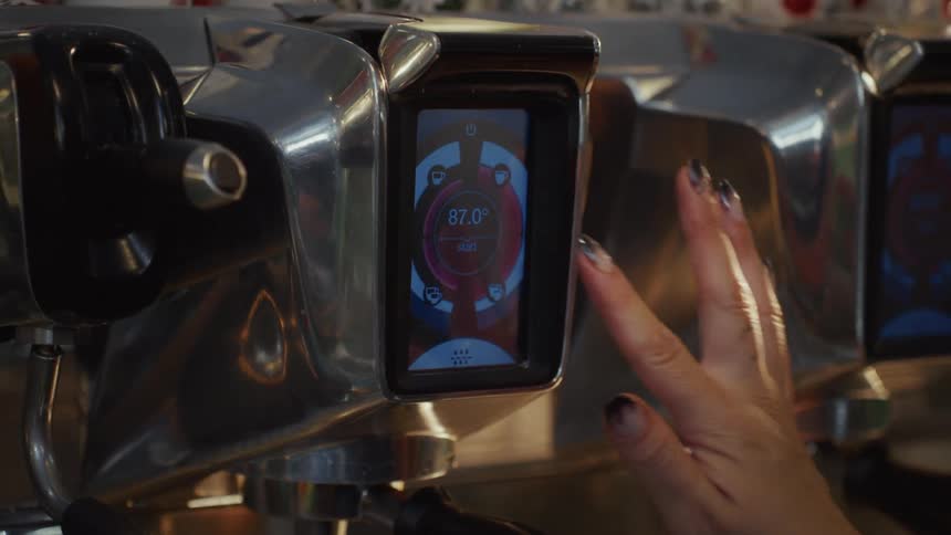 A barista's hand adjusts the digital settings on the touch screen of a professional espresso machine