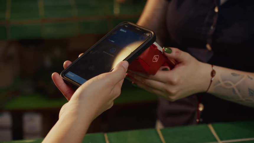 A customer makes a contactless payment by tapping their smartphone on a POS terminal held by a cashier