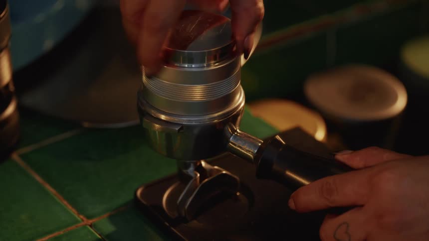 A close-up of a barista expertly using a coffee distributor to evenly prepare fresh espresso grounds in a portafilter