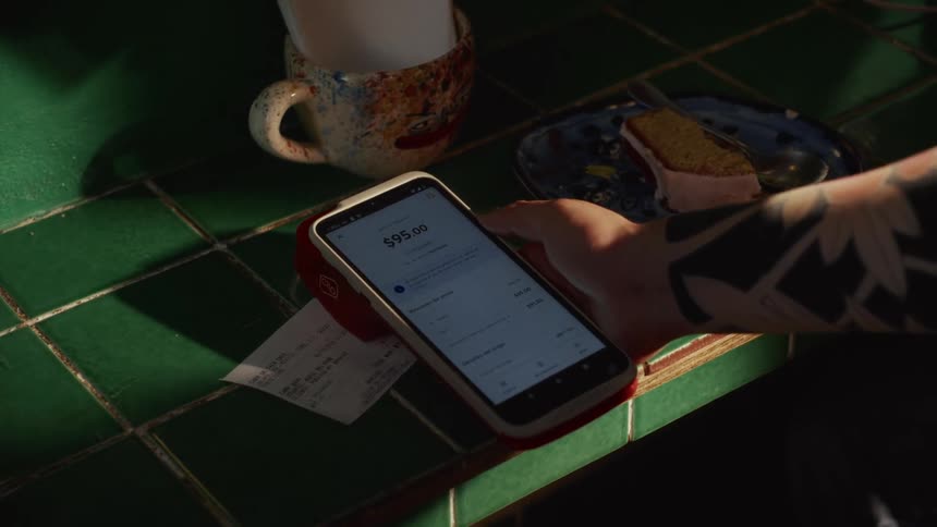 A customer makes a contactless payment with a credit card on a mobile POS terminal at a cafe counter