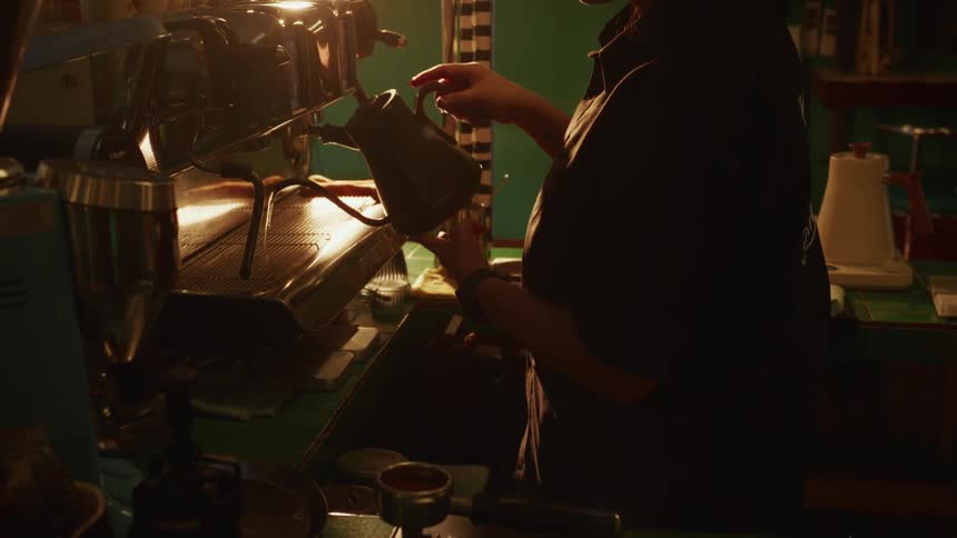 In a warmly lit and moody coffee shop, a barista skillfully prepares a coffee drink using an espresso machine