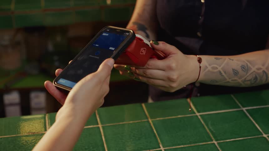 A customer makes a contactless payment by tapping their smartphone on a red card reader held by a cashier