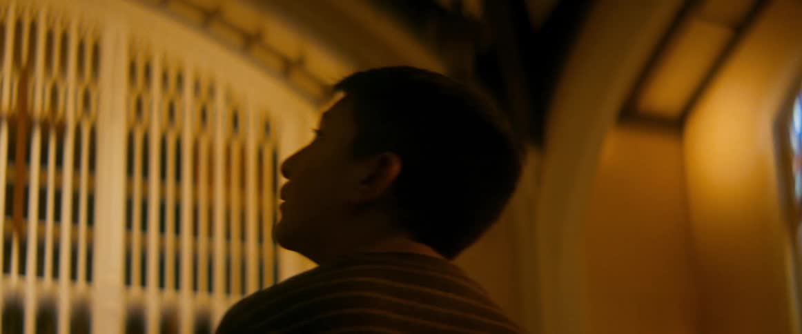 A young boy quietly walks through a dimly lit church, gazing in awe at the beautiful stained-glass windows and architecture