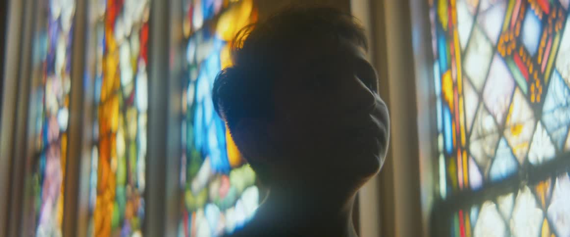 A young boy looks up in wonder, silhouetted against the colorful light of a stained glass window