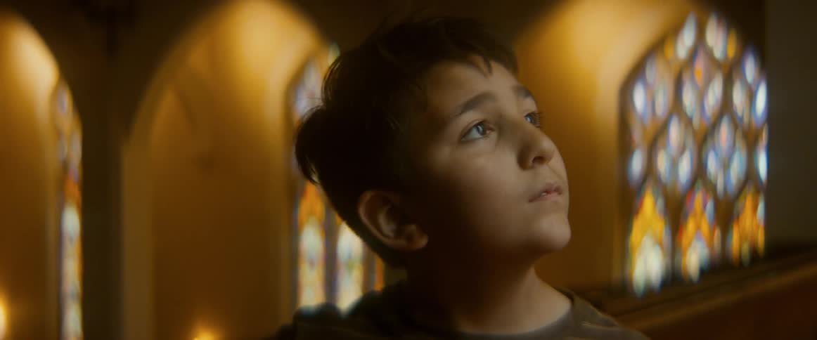A young boy with a look of awe and wonder on his face sits inside a warm, beautiful church