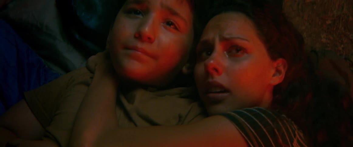 Worried mother holds frightened young son close while lying together in dim red light