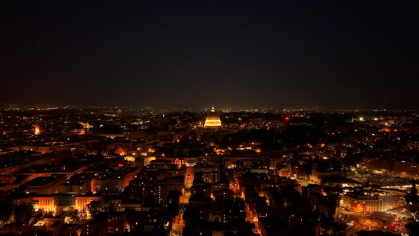 Stunning nighttime aerial drone shot flying over the illuminated city of Rome towards the iconic St. Peter's Basilica in Vatican City