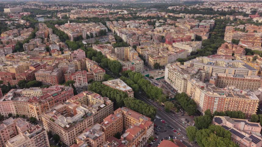 An expansive aerial view reveals the dense urban sprawl of Rome, showcasing tree-lined boulevards and classic European architecture with distant mountains on the horizon