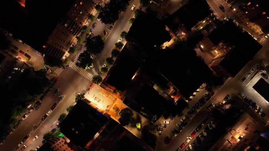 A serene top-down aerial view reveals a quiet European city at night, with streetlights illuminating the roads and building tops