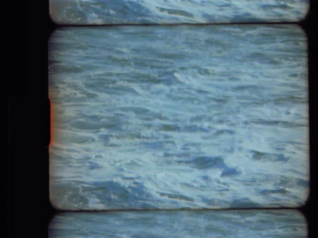 Archival 8mm film captures a static, close-up shot of churning and foamy ocean waves