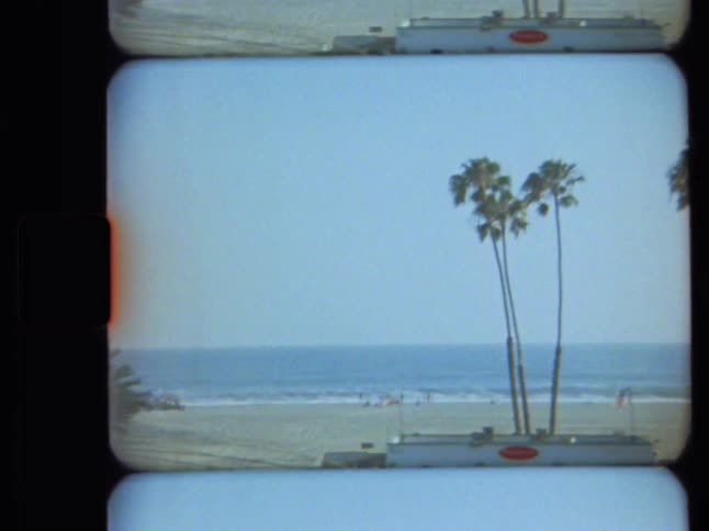Vintage 8mm film captures a woman jogging on a bridge leading to a sunny California beach with tall palm trees