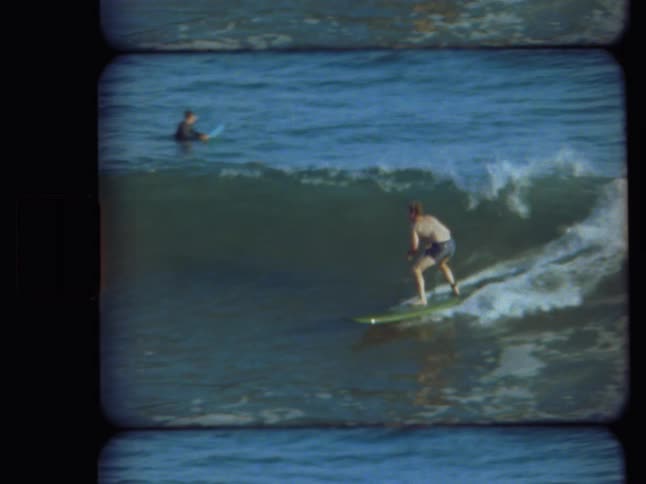 Vintage 8mm film footage captures a surfer riding a beautiful blue ocean wave before wiping out