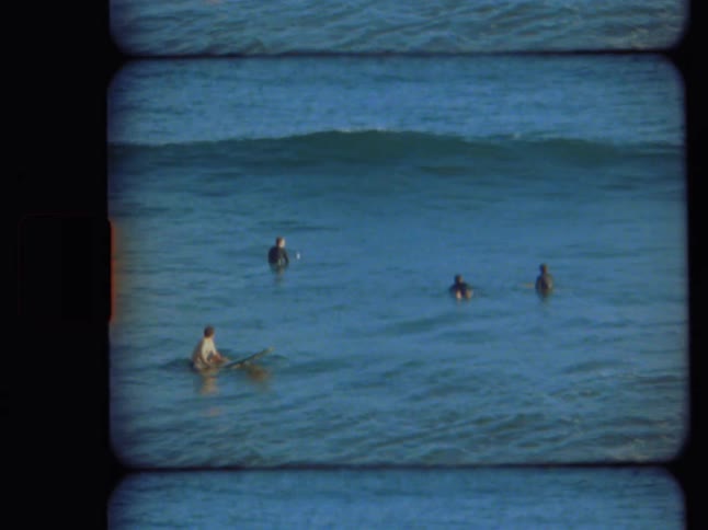 Authentic Super 8mm footage captures surfers waiting in the calm blue ocean for the next set of waves