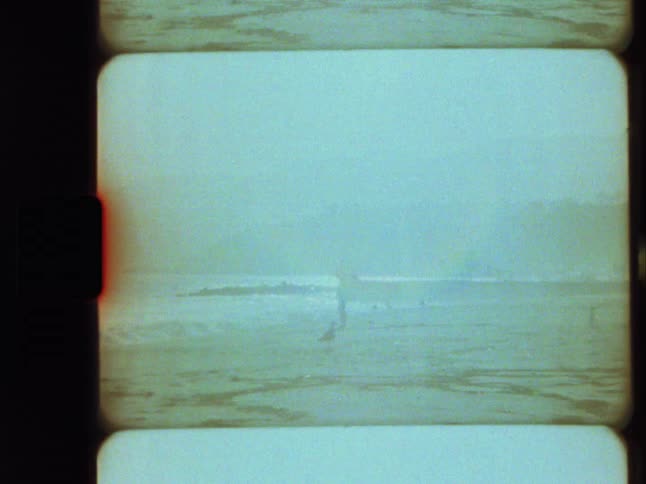 Vintage film captures hazy beach scenes of a lone figure by the ocean and a boombox on a picnic blanket