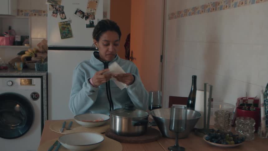 Slow motion footage shows a young woman at her kitchen table unfolding a napkin to wipe her nose