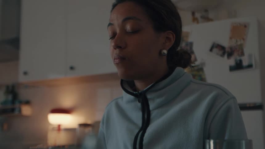 A young woman sits in her kitchen and mindfully savors a bite of food in slow motion