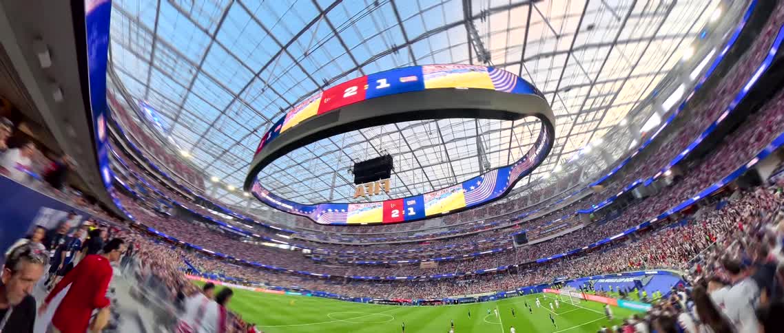 An immersive hyperlapse shot walks through the bustling crowd to reveal a breathtaking wide-angle view of a live FIFA football match in a state-of-the-art stadium