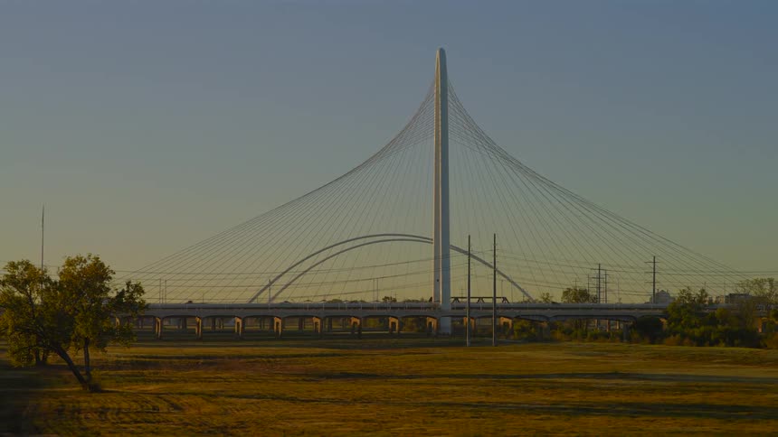 A serene tracking shot reveals the magnificent Margaret Hunt Hill Bridge in Dallas at sunrise, with traffic flowing peacefully across it