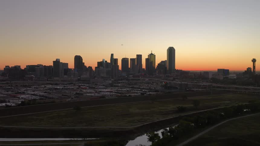 A slow aerial push towards the Dallas, Texas skyline as the city is silhouetted against a beautiful sunrise