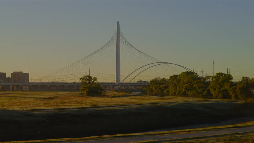 A tranquil, slow zoom-in on the iconic Margaret Hunt Hill Bridge in Dallas, Texas, bathed in the warm light of sunrise