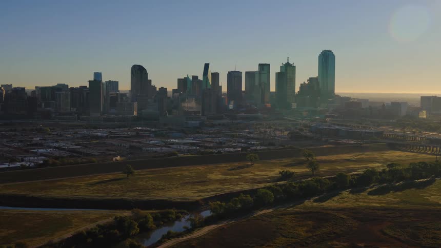 An aerial drone slowly flies towards the majestic Dallas, Texas skyline during a beautiful golden sunrise
