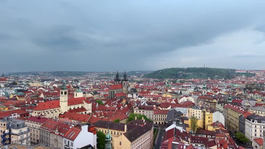 A slow aerial pullback reveals the sprawling cityscape of Prague with its iconic red rooftops under a moody, overcast sky