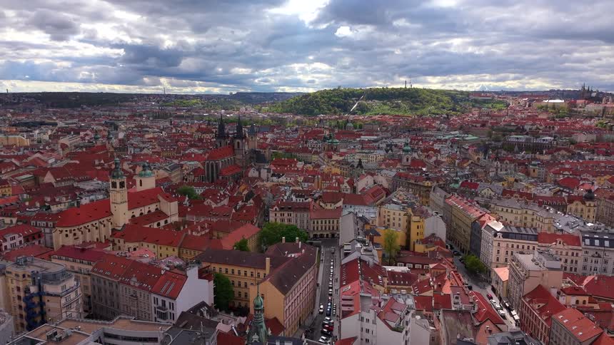 A slow aerial pullback reveals the historic old town of Prague, Czech Republic, with its iconic red-roofed cityscape under a cloudy sky