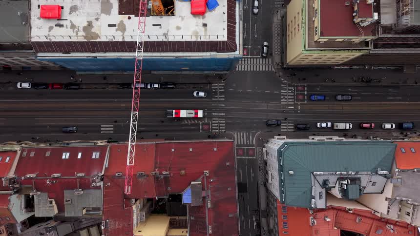 A top-down aerial view reveals the movement of cars, trams, and buses through a bustling city street surrounded by colorful historic buildings