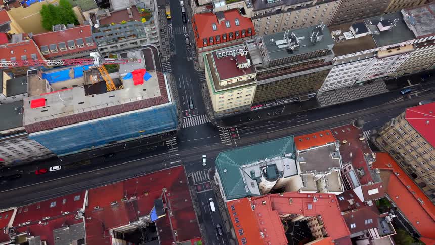 An aerial top-down view of a historic European city intersection with moving traffic among traditional red-roofed buildings