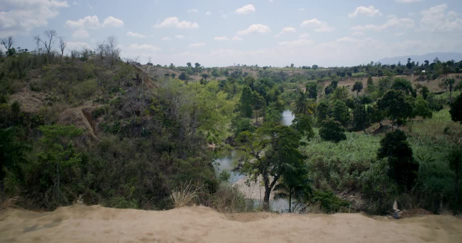 A slow push-in shot from a dry hilltop reveals a lush, green river valley surrounded by trees on a sunny day